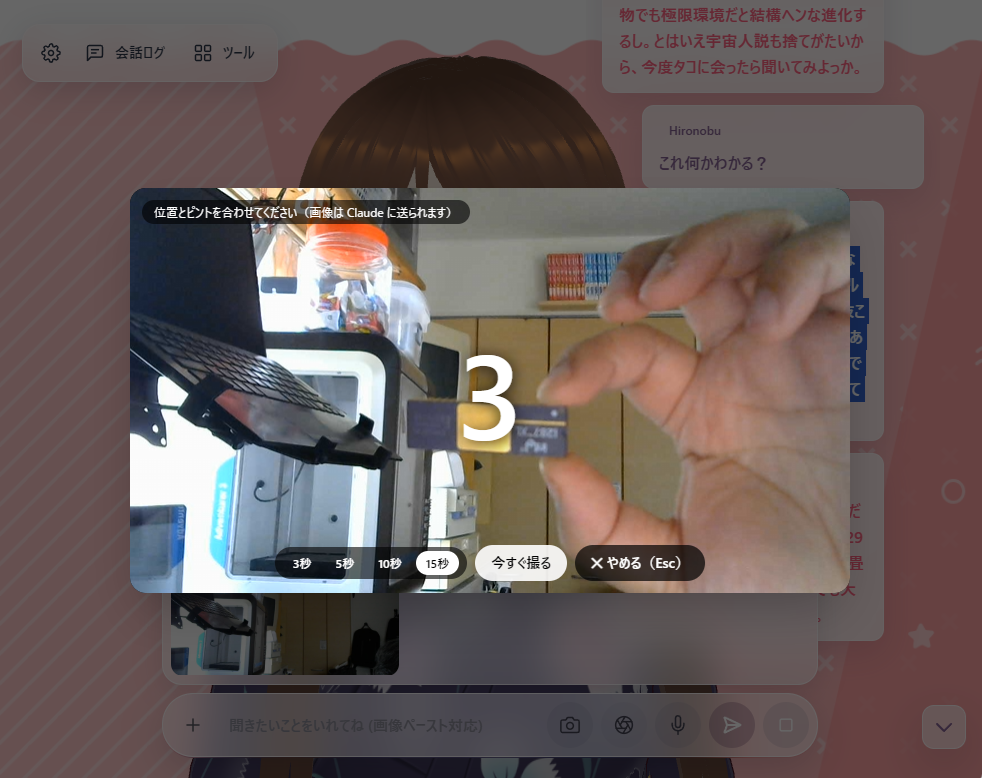 会話アプリの中央にカメラの映像が出て、指でつまんだ部品の上に大きく「3」とカウントダウンが表示されている。下に 3秒・5秒・10秒・15秒 の切り替えと「今すぐ撮る」「やめる」のボタン