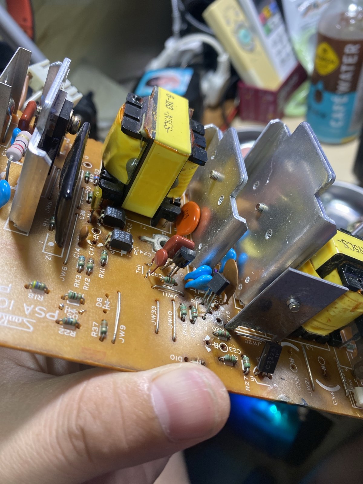 9801DX2 の電源基板を手に持って撮った写真。黄色いトランス、銀色の放熱板、NEC のフォトカプラ、茶色いはんだ面が写っている
