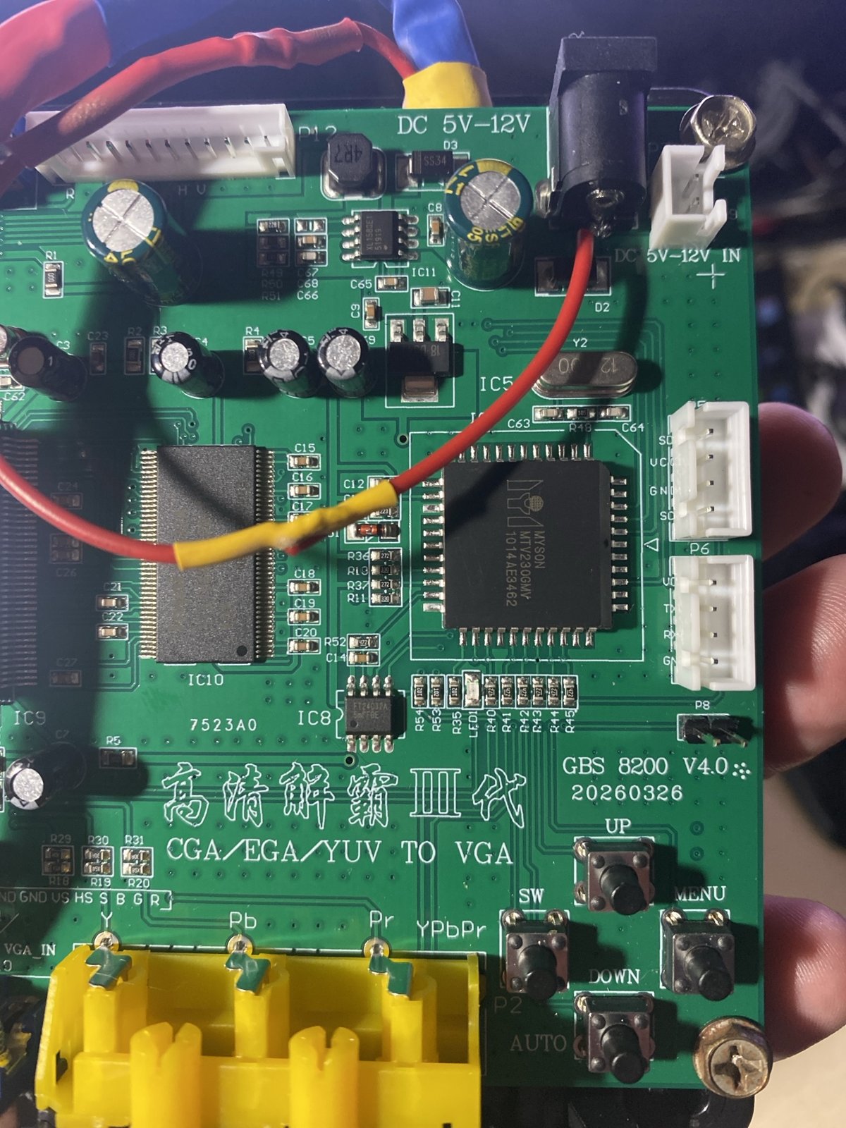 GBS-8200 V4.0 基板の右半分を手に持って撮った写真。基板に「GBS 8200 V4.0 20260326」の刻印、UP・MENU・DOWN・SW・AUTO のボタン、DC 5V-12V の電源ジャック、中央に MYSON の制御チップがある