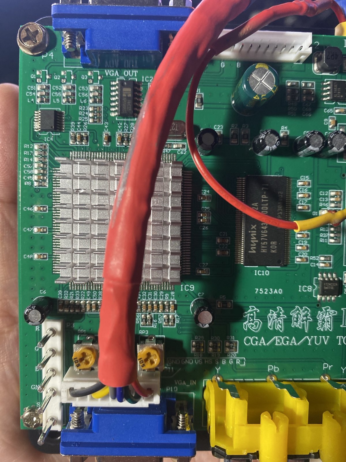 GBS-8200 基板の左下を手に持って撮った接写。P11 ヘッダに白いコネクタが挿さり、灰色・黄色・青・緑などの細い線が出ている。基板上の表示は GND GND VS HS S B G R。左に 2 つのオレンジ色の調整ツマミ、上に赤い太いケーブル